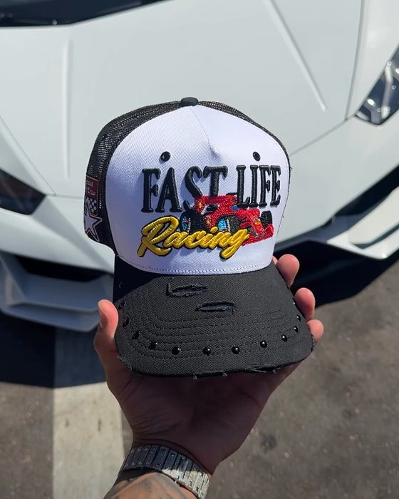 Fast Life Racing trucker held in a hand in front of a white sports car