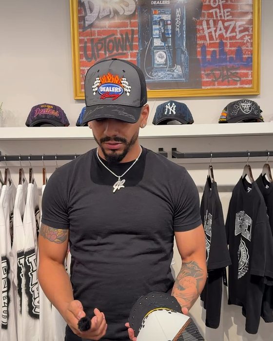 A Dealers team member in the shop holding a hat, with a wall of hats behind him